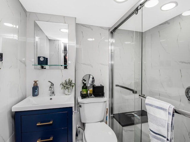 bathroom featuring vanity, toilet, a shower with door, and tile walls