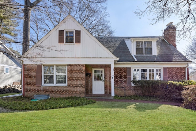 view of front of home featuring a shingled roof, a chimney, a front lawn, and brick siding