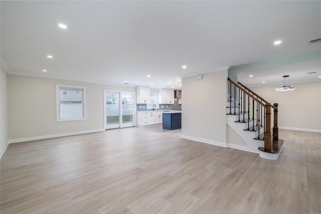 unfurnished living room featuring light wood-type flooring, ornamental molding, and sink