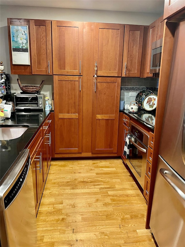 kitchen with backsplash, sink, stainless steel appliances, and light hardwood / wood-style flooring