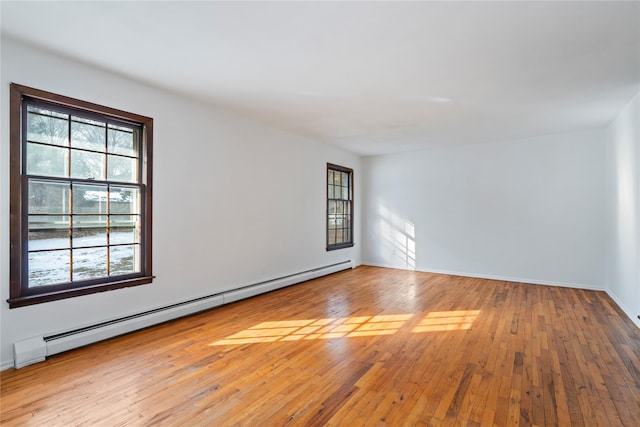 empty room with a wealth of natural light, light wood-type flooring, and a baseboard heating unit