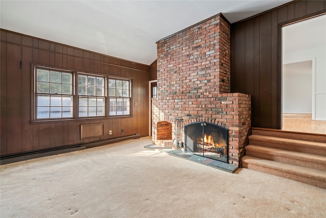 unfurnished living room with a baseboard radiator, wooden walls, light colored carpet, and a fireplace