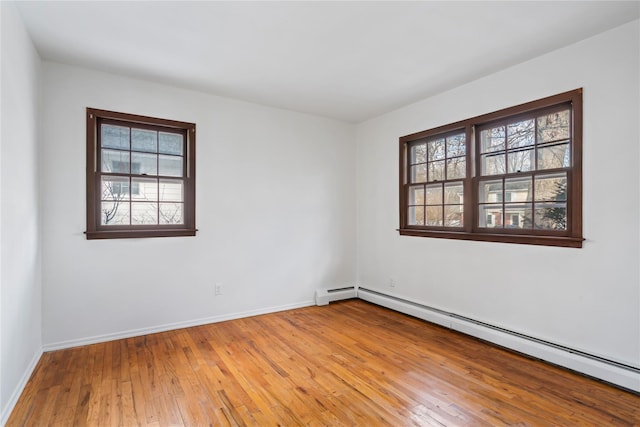 empty room featuring a baseboard heating unit, a wealth of natural light, and wood-type flooring