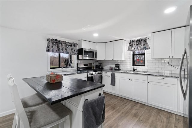 kitchen featuring white cabinets, sink, kitchen peninsula, wood-type flooring, and stainless steel appliances