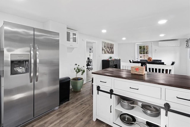 kitchen with wood counters, dark wood-type flooring, white cabinets, stainless steel fridge, and a wall unit AC