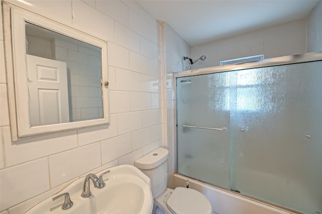 full bathroom featuring sink, toilet, combined bath / shower with glass door, and tile walls