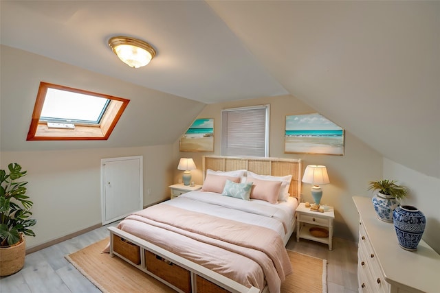 bedroom with lofted ceiling with skylight and light hardwood / wood-style flooring