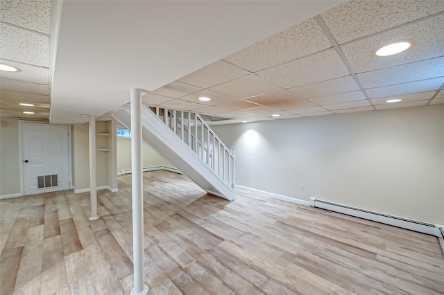 basement featuring hardwood / wood-style flooring, a baseboard heating unit, and a drop ceiling