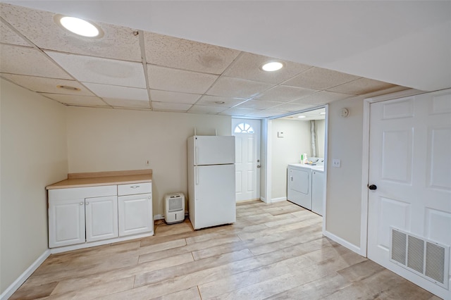 kitchen with a paneled ceiling, washing machine and dryer, white cabinetry, white refrigerator, and light wood-type flooring