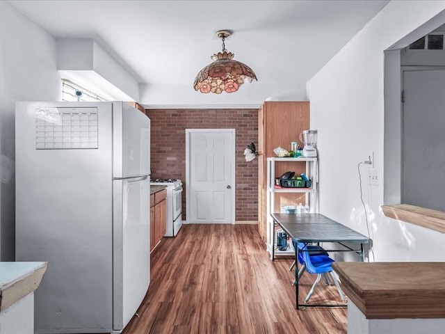 kitchen with decorative light fixtures, white appliances, dark wood-type flooring, and brick wall