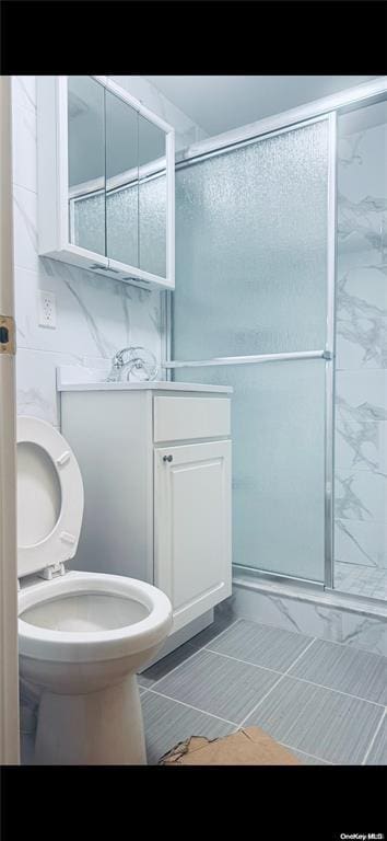 bathroom with tile patterned floors, walk in shower, vanity, tile walls, and toilet