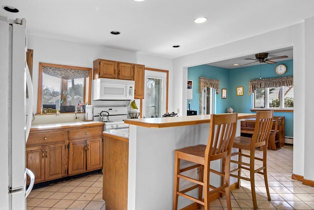 kitchen featuring white appliances, a kitchen breakfast bar, ceiling fan, light tile patterned floors, and a baseboard radiator