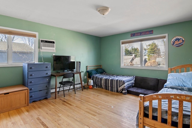 bedroom with a wall unit AC, baseboard heating, and light hardwood / wood-style floors