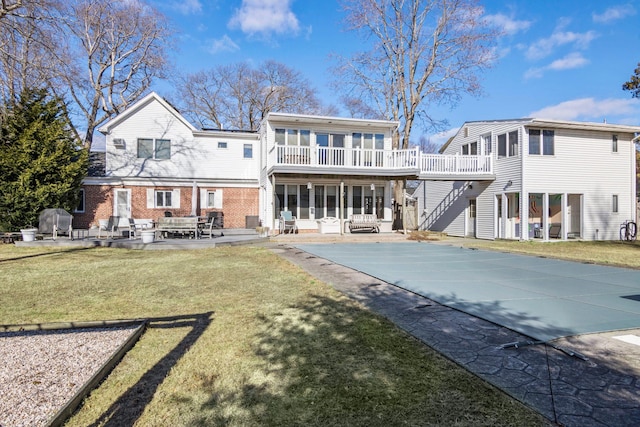 rear view of property featuring a lawn, a balcony, and a patio