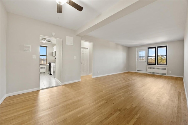 empty room featuring ceiling fan, radiator, and light hardwood / wood-style flooring