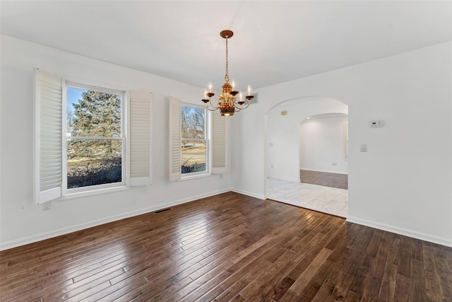 unfurnished dining area featuring hardwood / wood-style floors, a notable chandelier, arched walkways, and visible vents