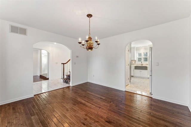 empty room with visible vents, hardwood / wood-style flooring, arched walkways, baseboards, and stairs