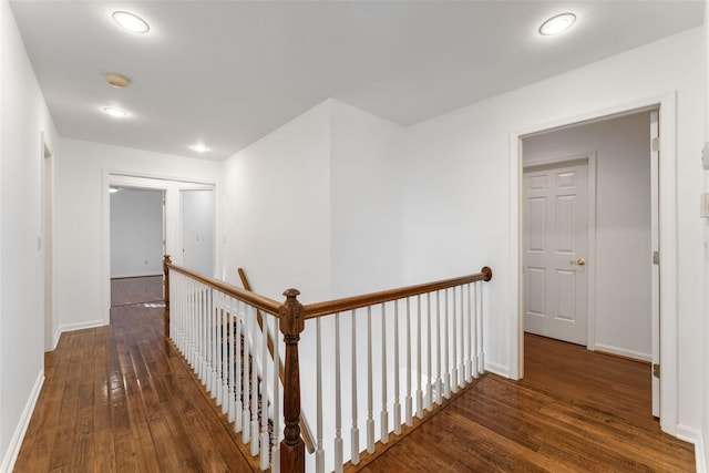 hall with an upstairs landing, baseboards, and wood-type flooring