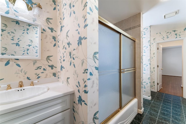 bathroom with combined bath / shower with glass door, vanity, and wallpapered walls