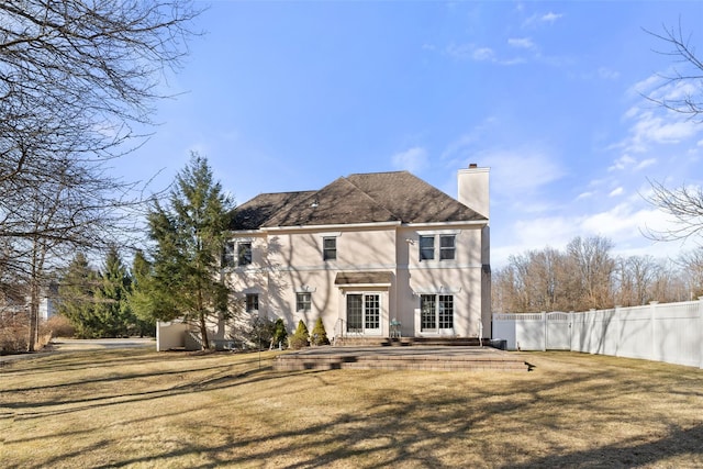 rear view of property featuring stucco siding, a yard, fence, and a chimney