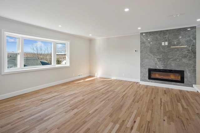 unfurnished living room featuring ornamental molding, a fireplace, and light hardwood / wood-style flooring