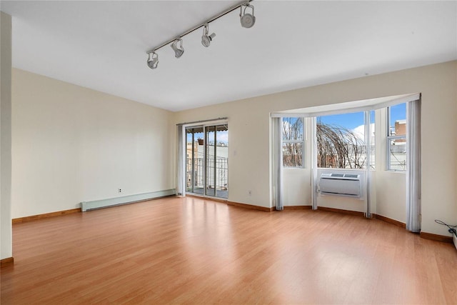 empty room with track lighting, an AC wall unit, light hardwood / wood-style flooring, and a baseboard radiator