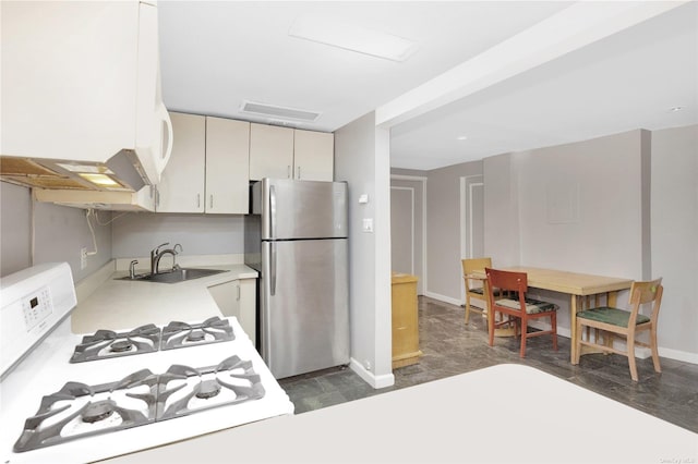 kitchen with stainless steel fridge, cream cabinets, white gas range, and sink