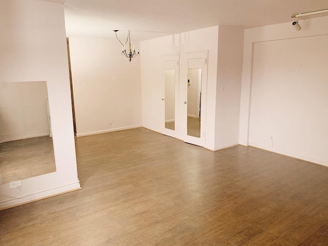 spare room with a chandelier, track lighting, and wood-type flooring