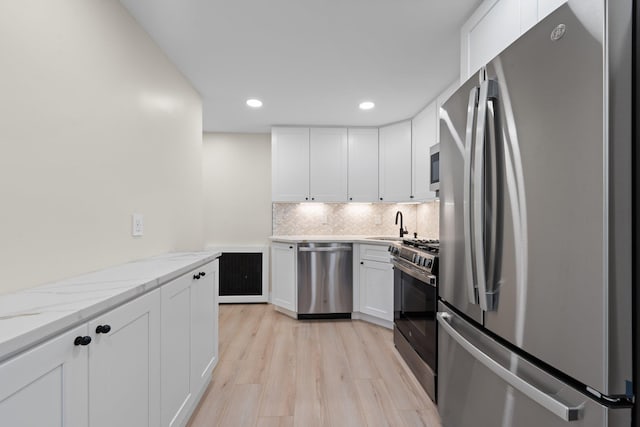 kitchen with light stone countertops, white cabinetry, appliances with stainless steel finishes, and light wood-type flooring