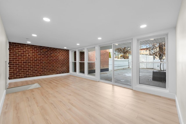 spare room with light wood-type flooring and brick wall