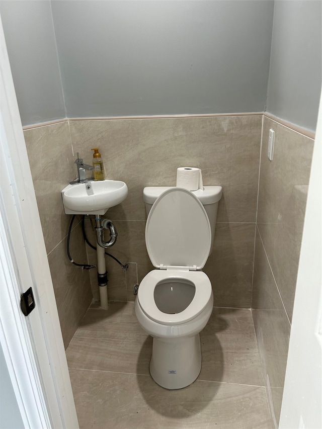 bathroom with tile patterned flooring, toilet, sink, and tile walls