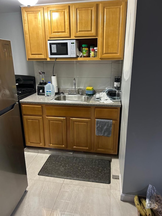 kitchen with decorative backsplash, light tile patterned floors, stainless steel refrigerator, and sink