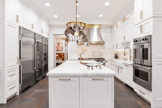 kitchen with white cabinetry, appliances with stainless steel finishes, a center island with sink, and wall chimney exhaust hood