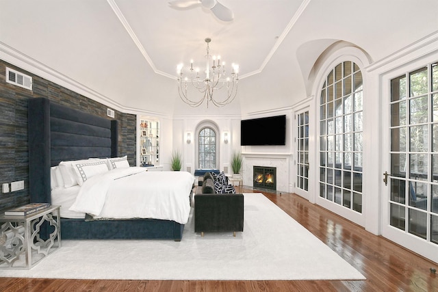 bedroom featuring a raised ceiling, wood-type flooring, a high end fireplace, crown molding, and ceiling fan with notable chandelier