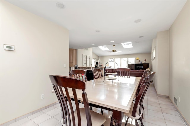 dining area with ceiling fan, a skylight, and light tile patterned floors