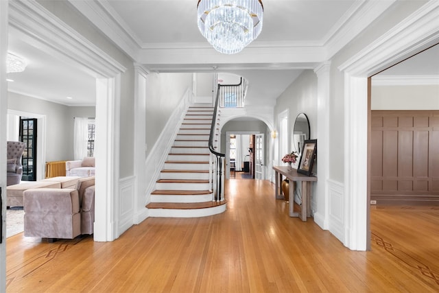 entryway with light wood-style floors, stairs, arched walkways, and crown molding