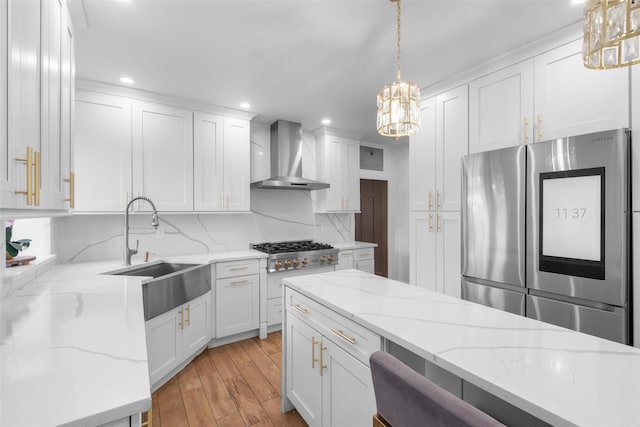 kitchen featuring decorative light fixtures, appliances with stainless steel finishes, white cabinets, a sink, and wall chimney range hood