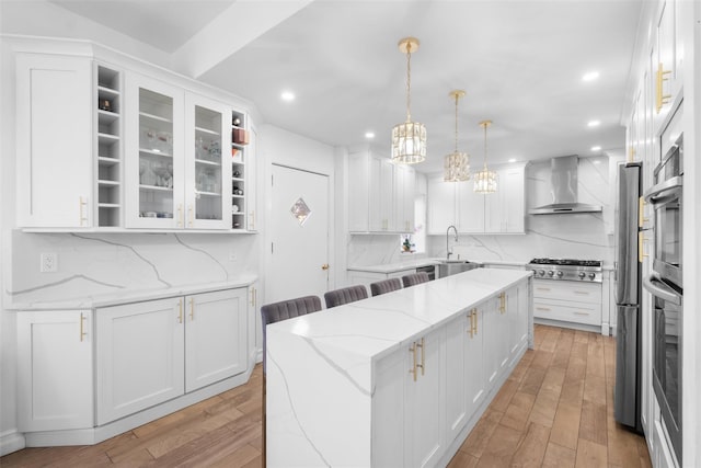 kitchen with glass insert cabinets, white cabinets, wall chimney range hood, and light stone counters