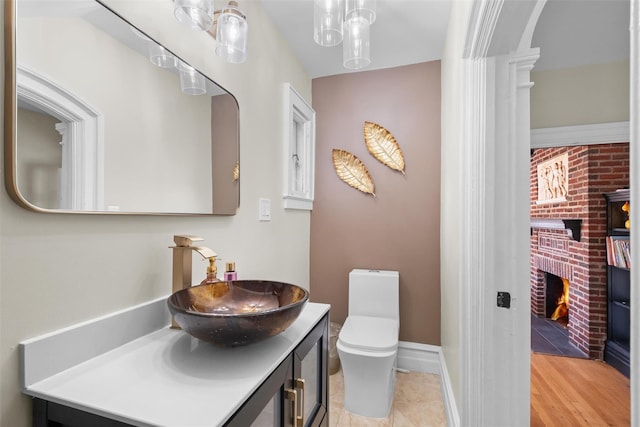 half bath featuring baseboards, a fireplace, vanity, and toilet