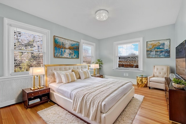 bedroom featuring baseboards, multiple windows, light wood-type flooring, and radiator