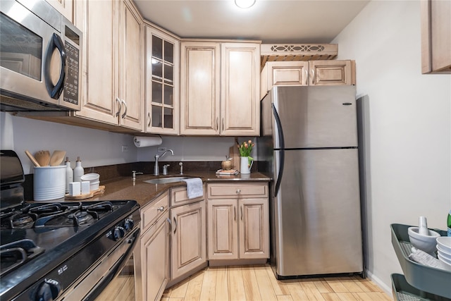 kitchen featuring light brown cabinets, sink, stainless steel appliances, dark stone countertops, and light wood-type flooring