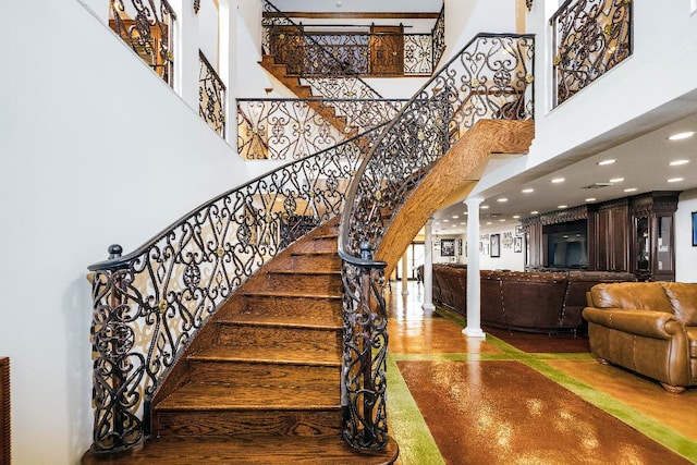 stairway with a towering ceiling, ornate columns, concrete flooring, and recessed lighting