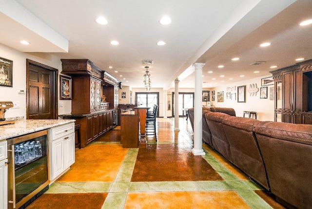 kitchen with dark brown cabinets, wine cooler, ornate columns, white cabinets, and a breakfast bar area