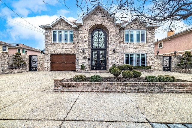 traditional-style home featuring stone siding, french doors, driveway, and an attached garage