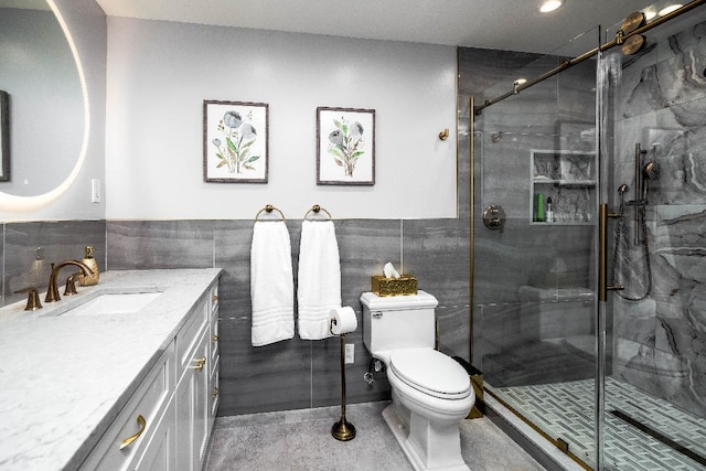 bathroom with vanity, toilet, tile walls, and a shower with door