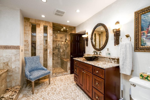 bathroom with tile walls, visible vents, toilet, a tile shower, and vanity