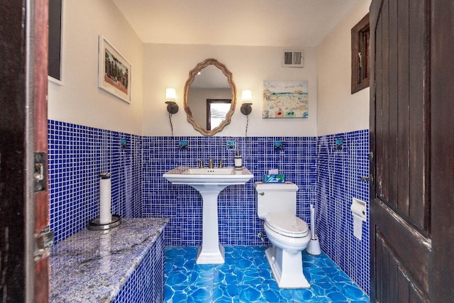 bathroom featuring toilet, a wainscoted wall, visible vents, and tile walls