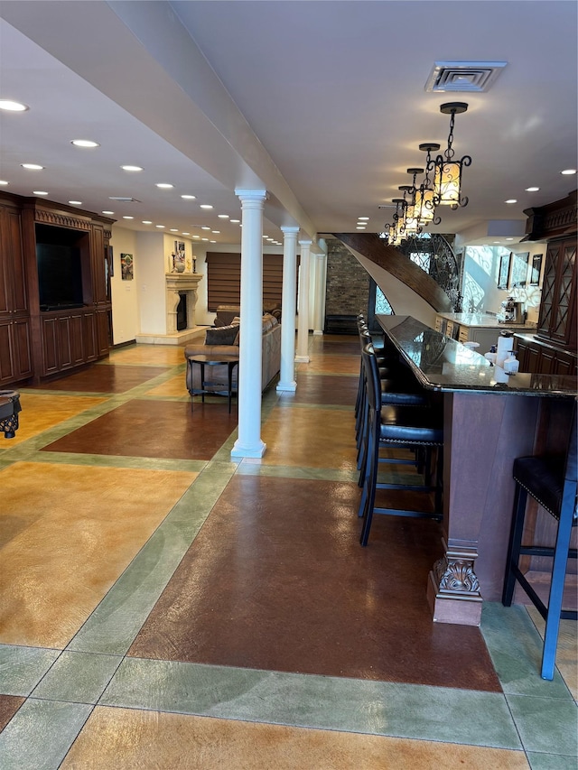 interior space featuring ornate columns, visible vents, open floor plan, and a kitchen bar