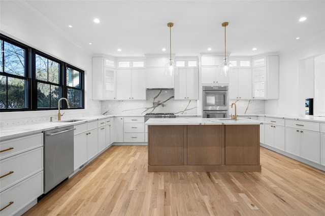 kitchen with stainless steel appliances, an island with sink, hanging light fixtures, light stone counters, and white cabinetry