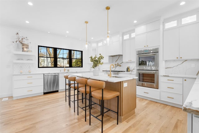 kitchen with pendant lighting, white cabinetry, stainless steel appliances, light stone countertops, and an island with sink